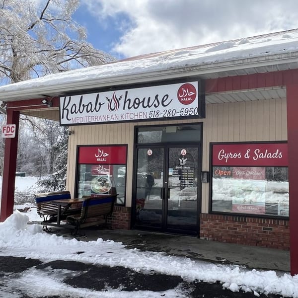 The Kabab House Mediterranean Kitchen storefront covered in snow, with outdoor benches and a clear blue sky.